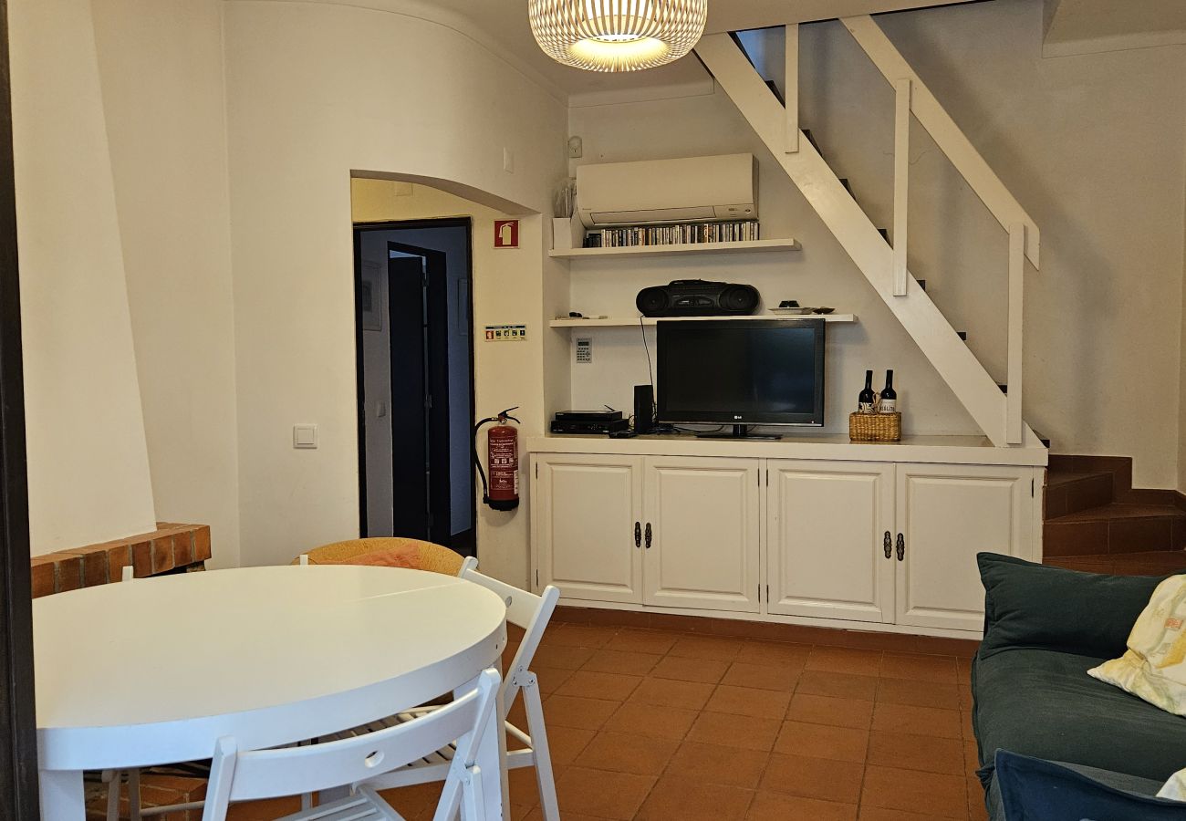 Sala de estar aconchegante com bancada, mesa de jantar e escada para o andar superior.