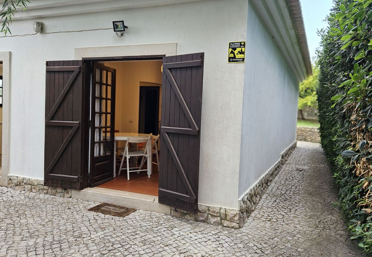 Fachada exterior, com portas de madeira e caminho rodeado por vegetação. 