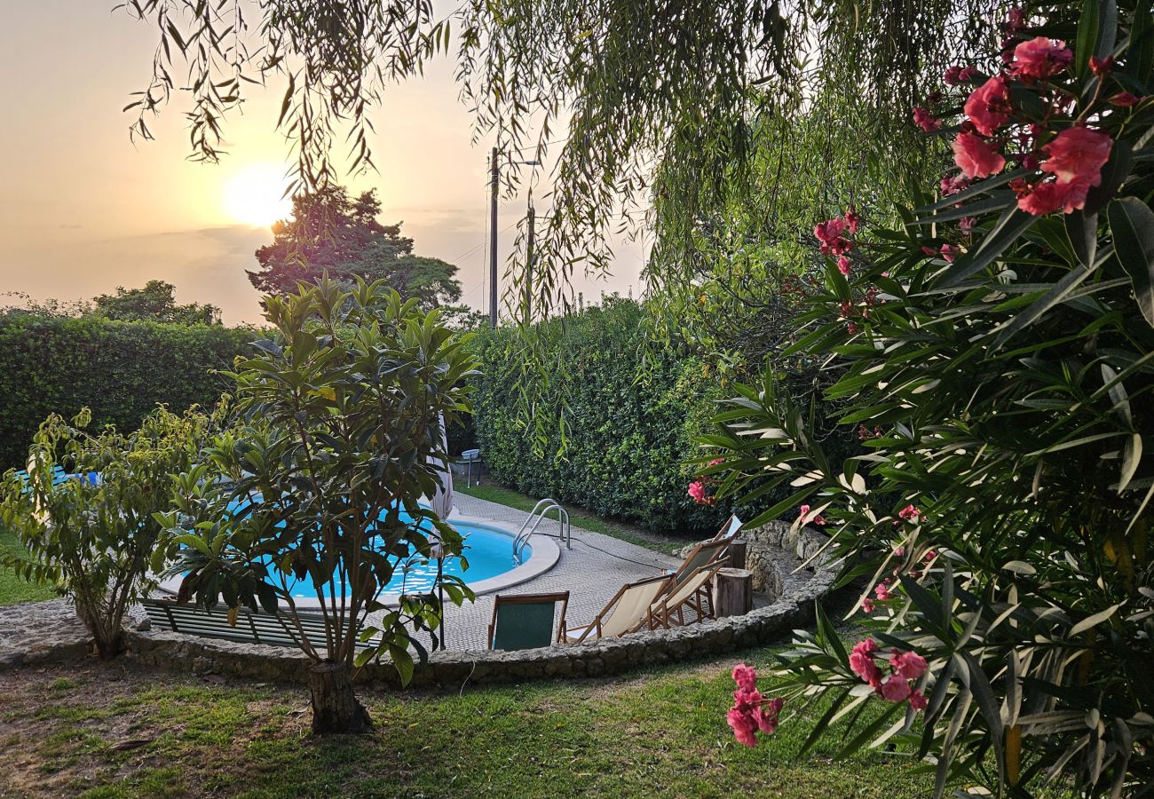 Tranquilo jardim de uma villa privada com piscina, cercado por vegetação exuberante e flores, ao fundo um belo pôr do sol dourado.