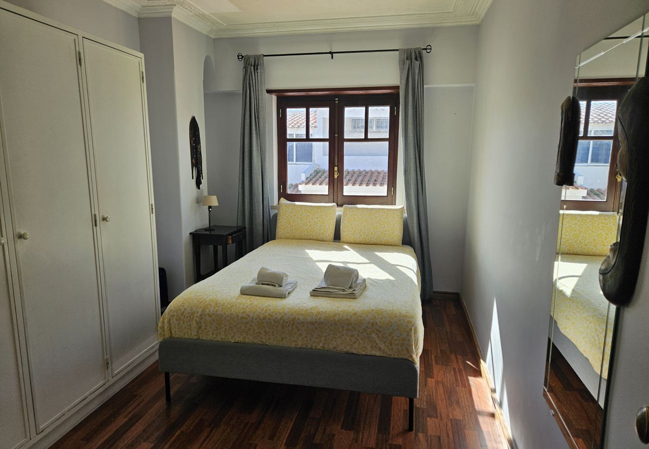 Quarto acolhedor com cama de casal, lençóis claros e janela com vista para a cidade.