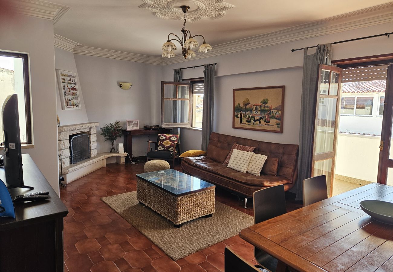Sala aconchegante com sofá, mesa de centro e portas de vidro para a varanda.