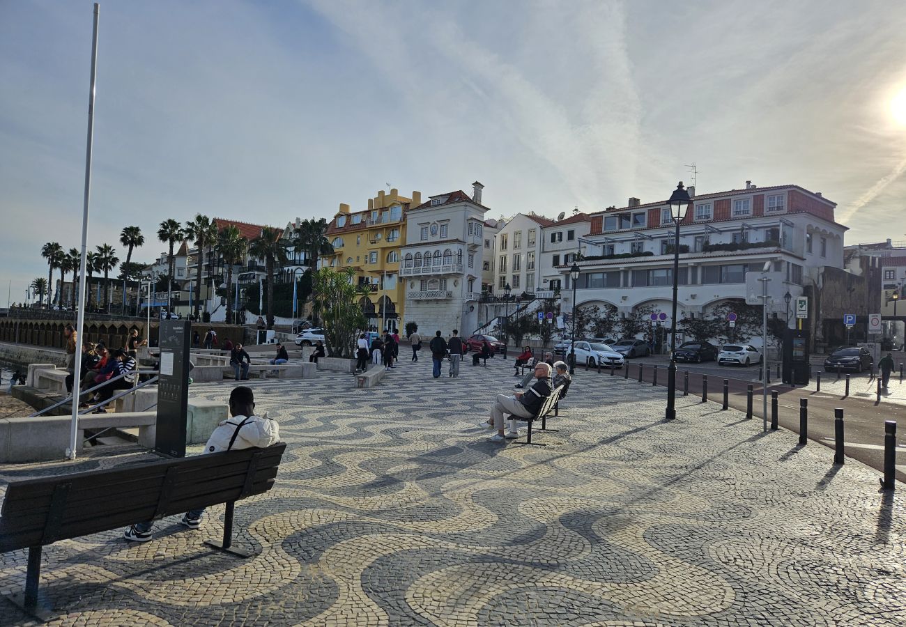 Avenida à beira-mar em Cascais, com calçadão, palmeiras e uma vista espetacular do oceano azul. 