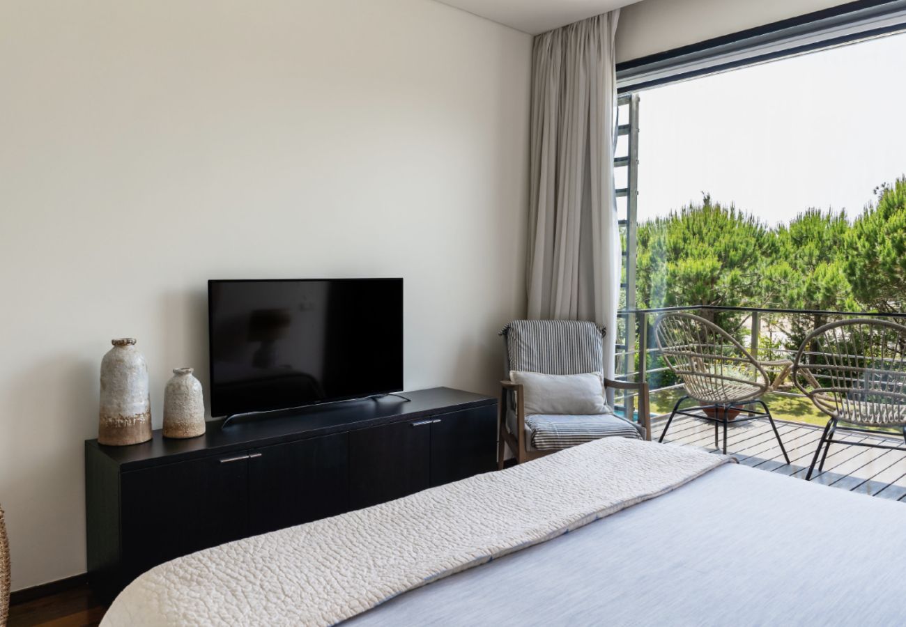 Quarto confortável com cama, TV, poltrona e acesso ao terraço com vista para a natureza na Pool Beach & Golf Troia.