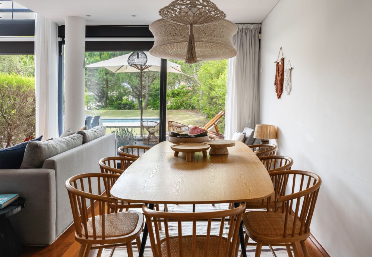 Sala de jantar aconchegante com mesa de madeira decorada e vista para o jardim na Pool Beach & Golf Troia.