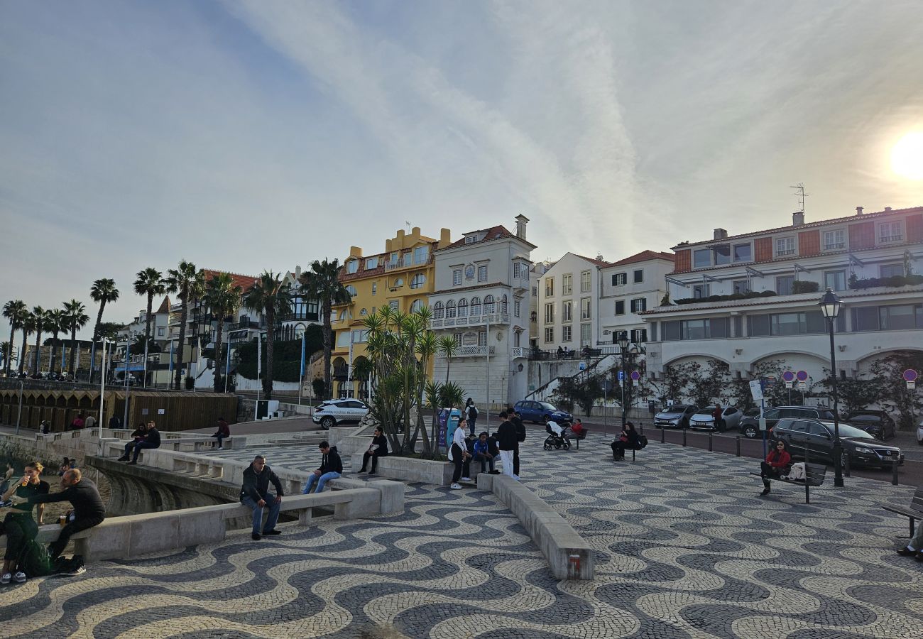 Caminho à beira-mar em Cascais, com vista para o oceano, palmeiras e a tradicional calçada portuguesa.