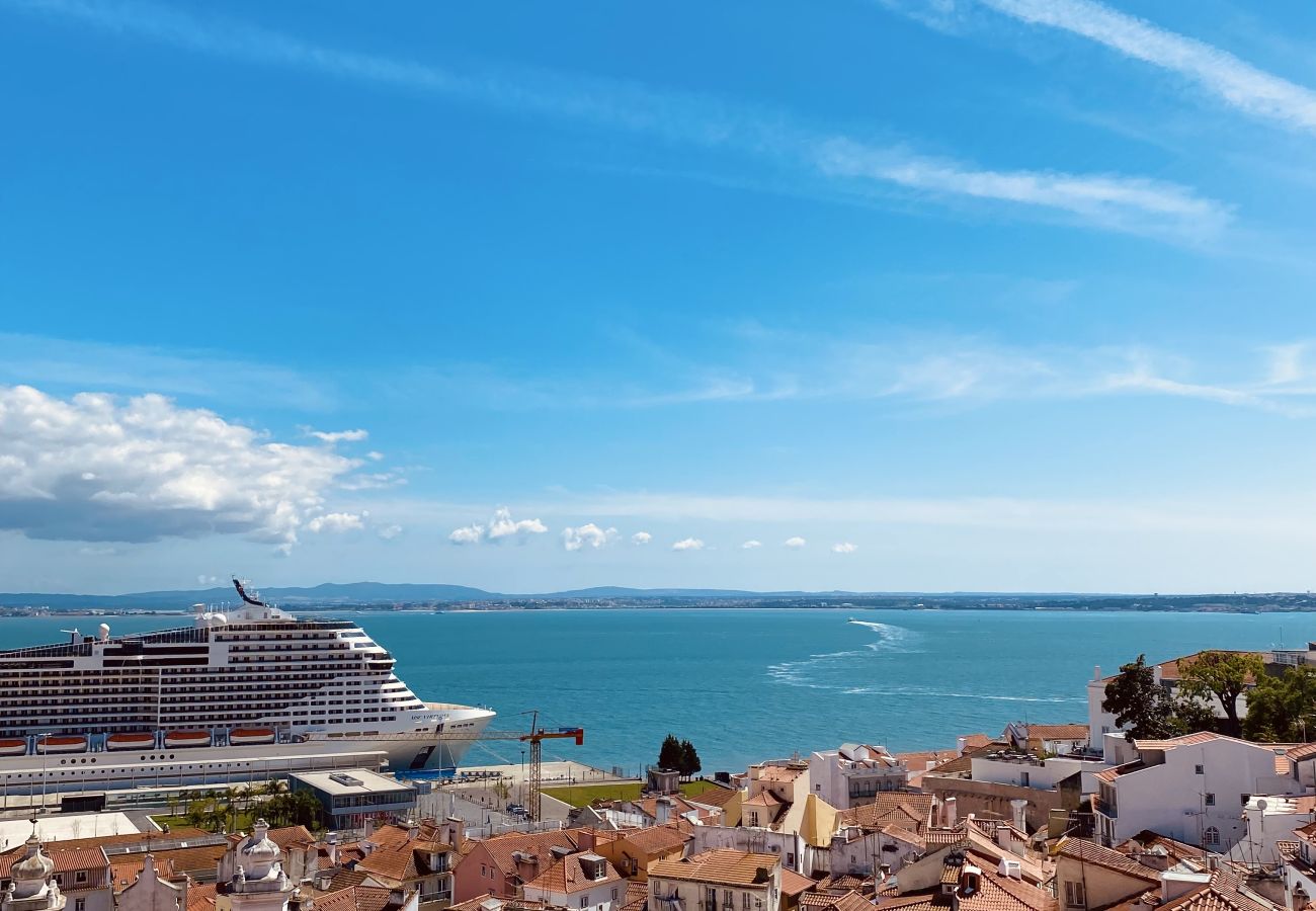 Vista aérea dos telhados históricos de Lisboa com o Rio Tejo ao fundo e um cruzeiro ancorado.