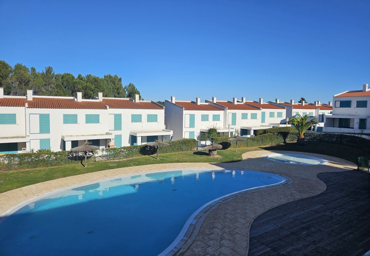 Vista panorâmica da piscina com espreguiçadeiras e casas de fachada branca e azul ao fundo.