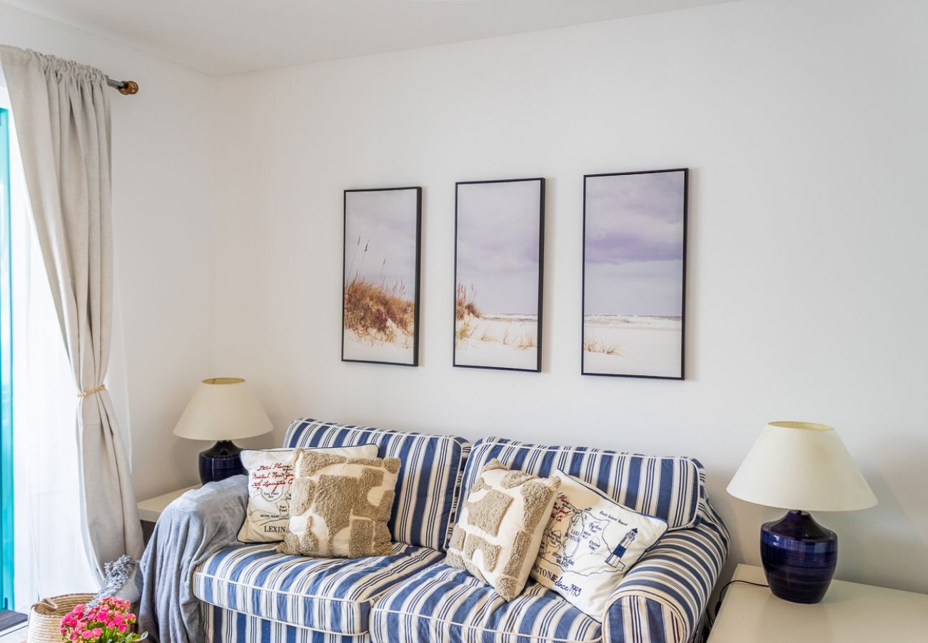 Sala de estar com sofá listrado azul e branco, almofadas decorativas, luminária e três quadros de paisagem na parede.