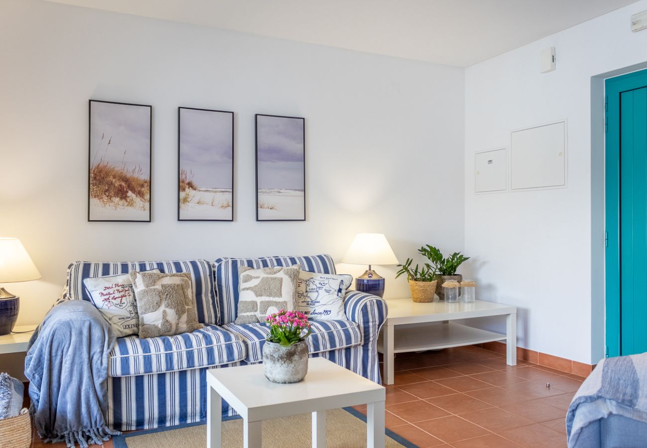 Sala com sofá azul, televisão e janelas amplas com luz natural.