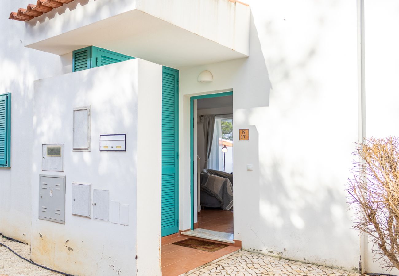 Fachada branca de uma casa com portas e janelas de madeira pintadas de azul-turquesa. A entrada está aberta, revelando parte da sala de estar.