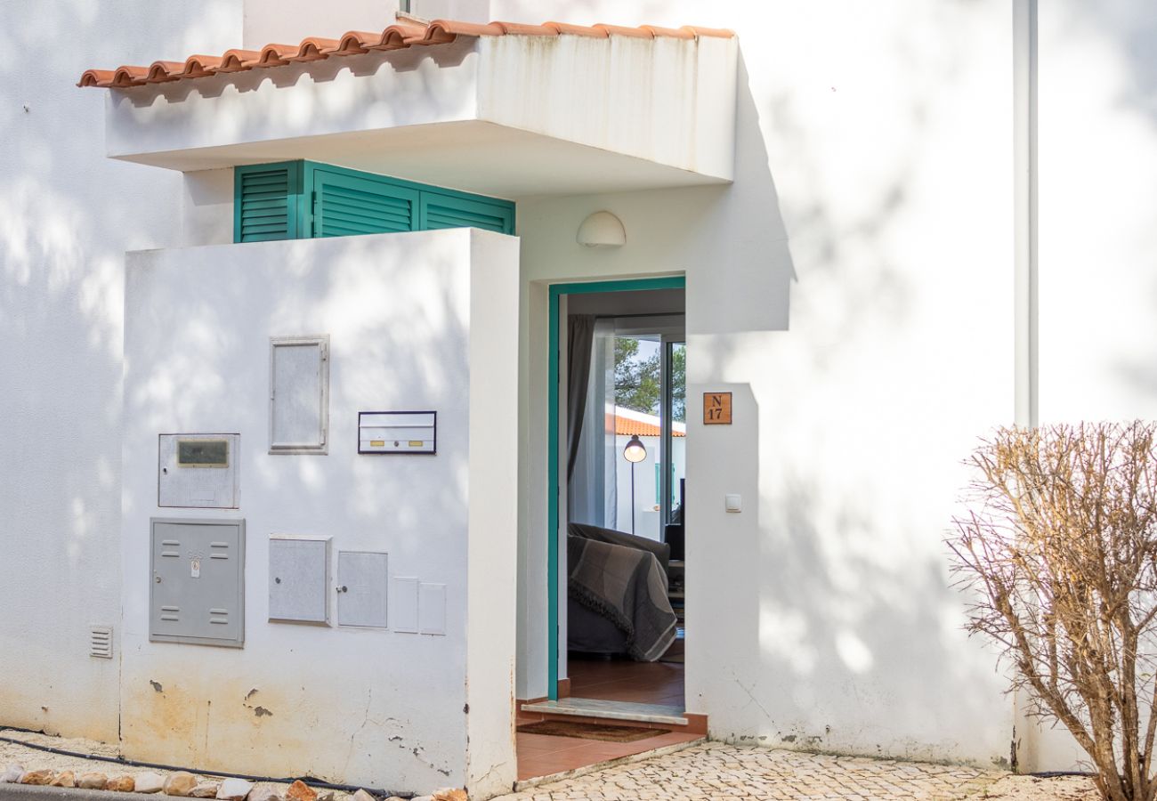 Entrada de uma casa branca com detalhes em azul-turquesa, incluindo portas e janelas. Pequeno telhado sobre a entrada e caixas de correio fixadas na p