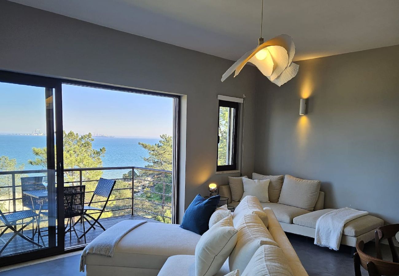 Sala de estar elegante com sofá grande, mesas de centro e varanda com vista para o mar.