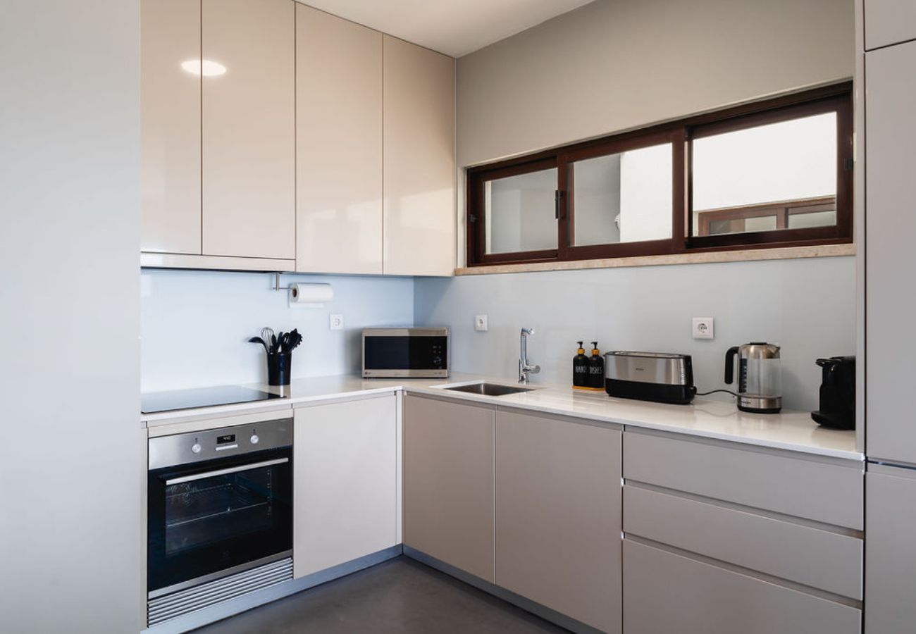 Cozinha compacta e moderna com eletrodomésticos embutidos, bancadas claras e armários elegantes.