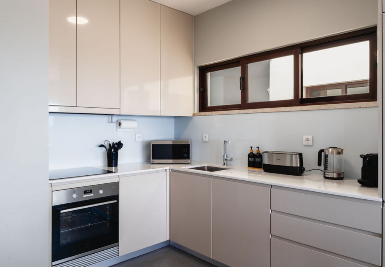 Cozinha elegante em tons neutros, equipada com eletrodomésticos embutidos, bancadas amplas e armários planejados.