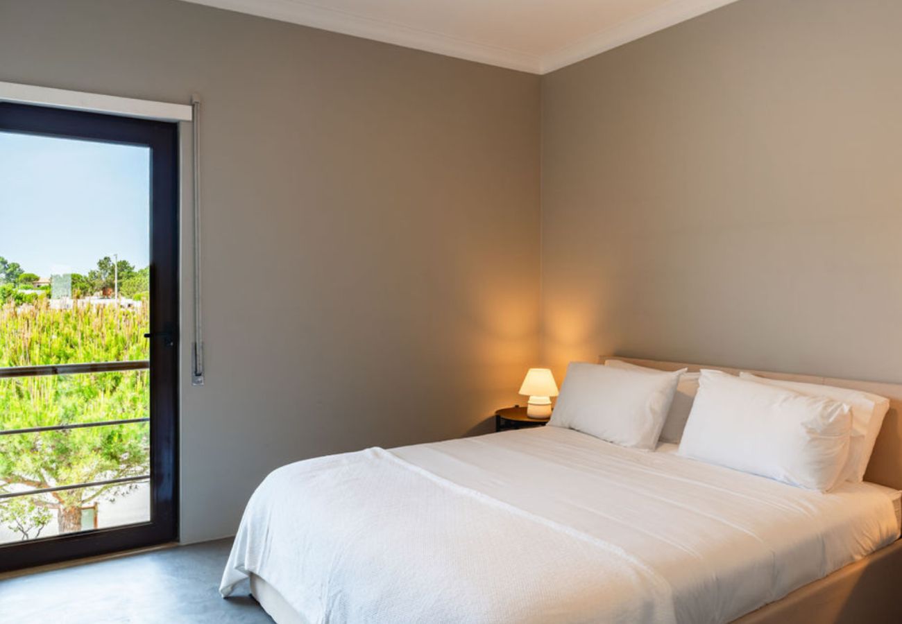 Quarto elegante com cama espaçosa, iluminação acolhedora e vista para a natureza através de uma grande janela.