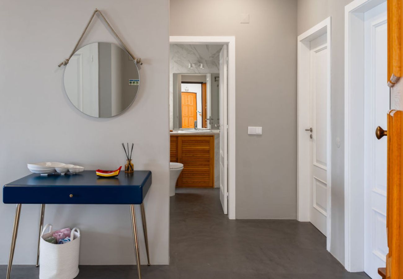 Hall de entrada moderno com mesa azul decorada, espelho redondo pendurado e acesso a diferentes cômodos, incluindo banheiro ao fundo.