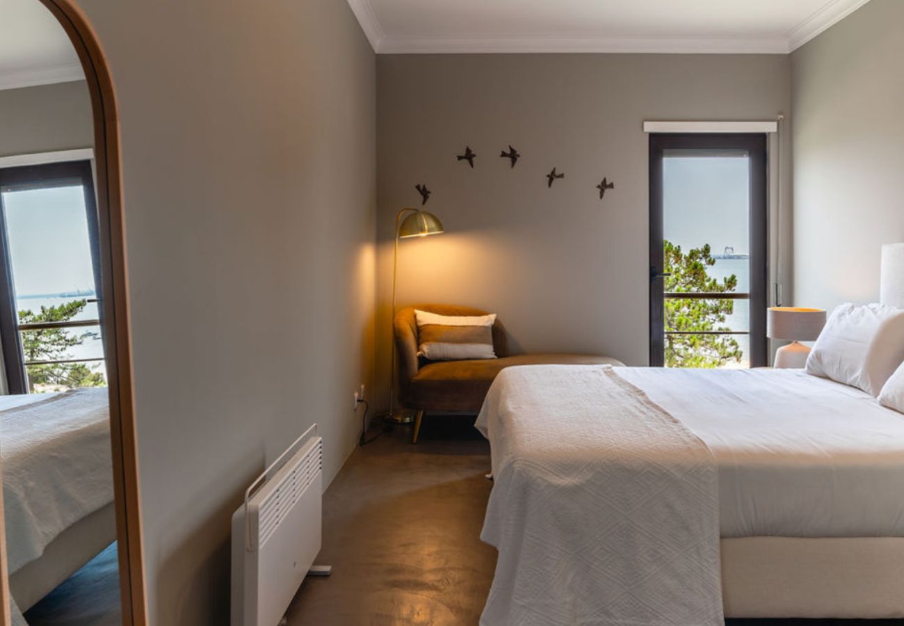 Quarto elegante com cama confortável, espelho grande e varanda com vista para o mar, decorado com tons neutros e iluminação suave.