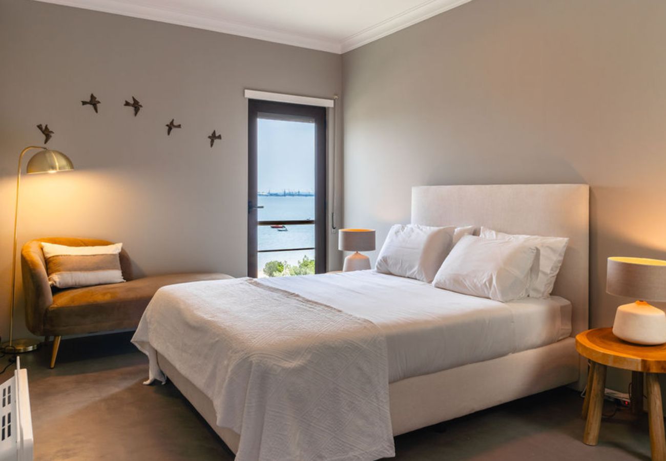 Quarto sofisticado com cama confortável, iluminação suave e varanda com vista deslumbrante para o mar e paisagem natural.
