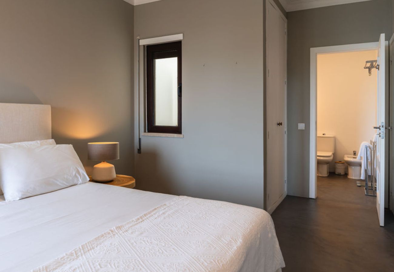 Quarto sofisticado com cama ampla, roupa de cama branca e suíte integrada, decorado em tons neutros e iluminação suave.