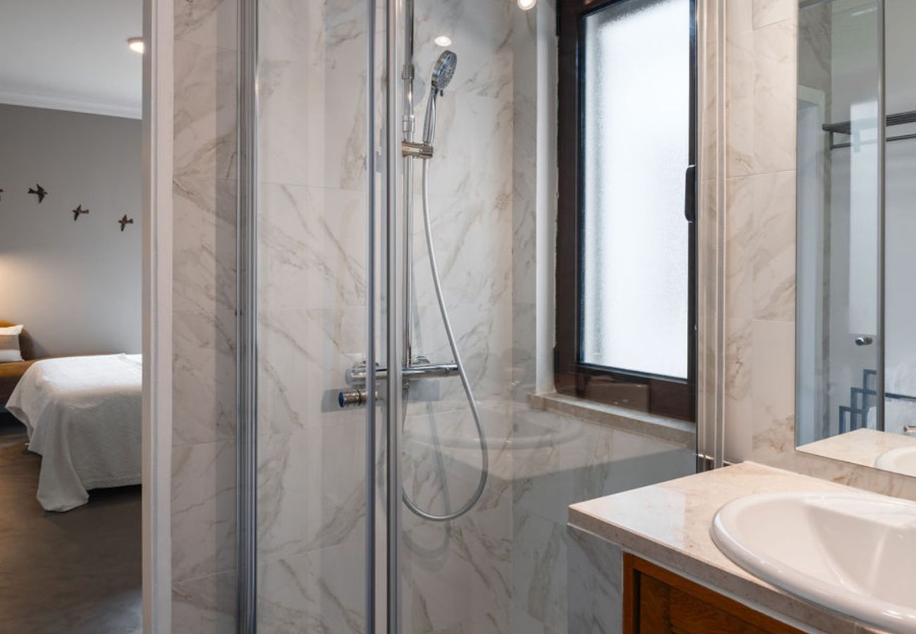 Banheiro elegante com revestimento em mármore, box de vidro com chuveiro e pia com bancada espaçosa e espelho amplo.
