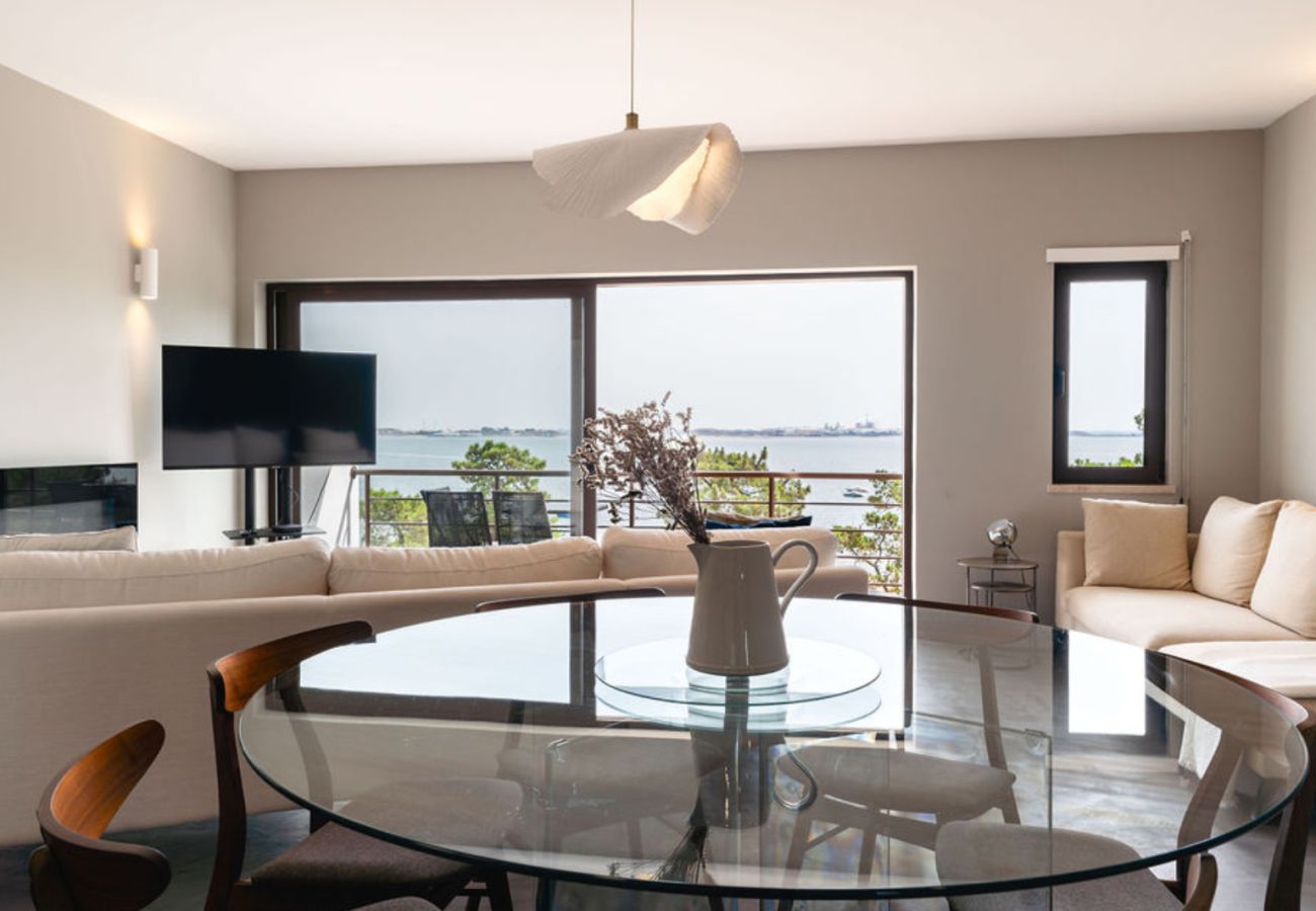 Sala de jantar elegante com mesa de vidro, cadeiras sofisticadas e janelas amplas com vista panorâmica para o rio.
