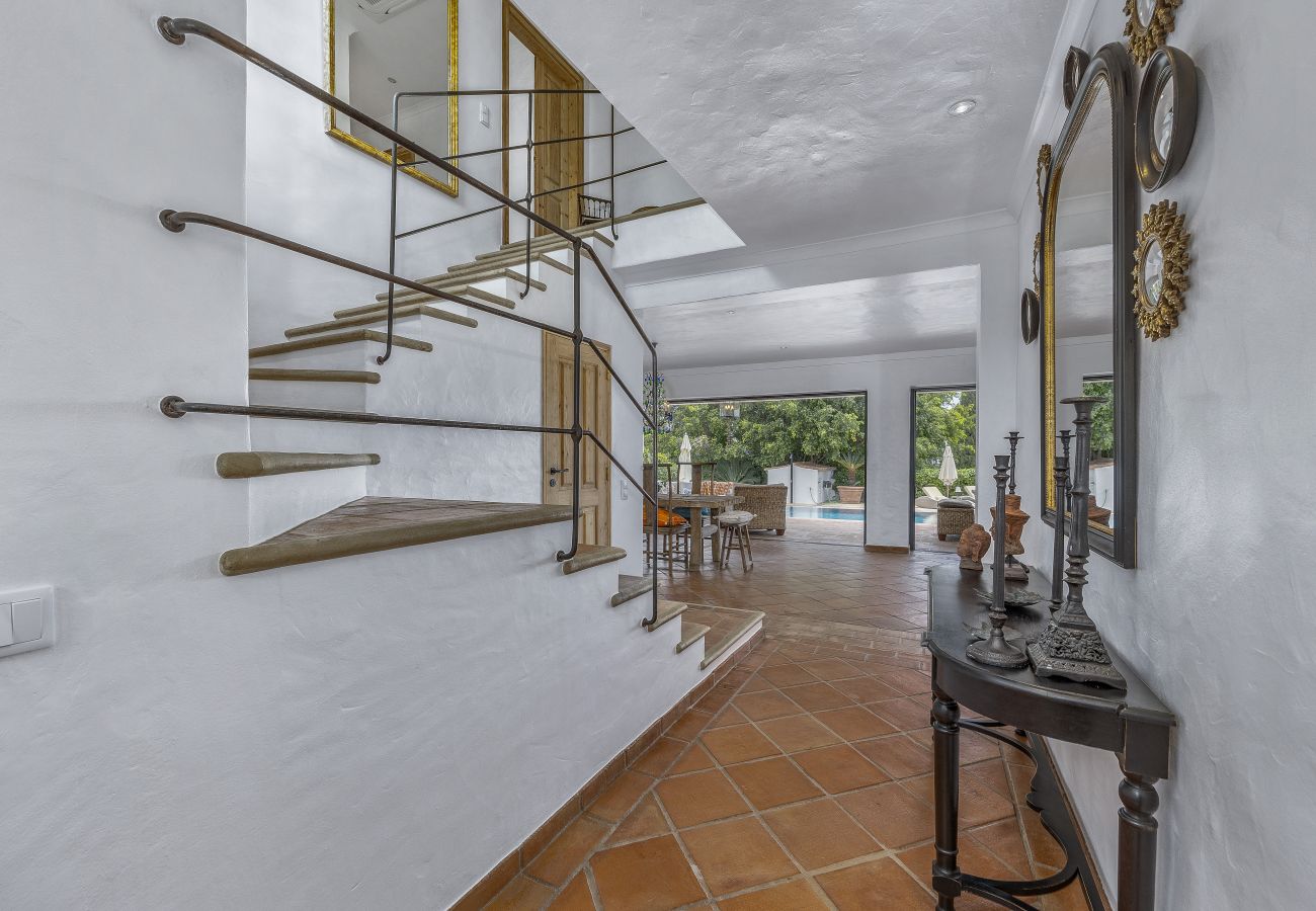 Elegante hall de entrada com escada moderna em espiral, mesa decorativa e espelho clássico, conduzindo para a sala de jantar e áreas exteriores.