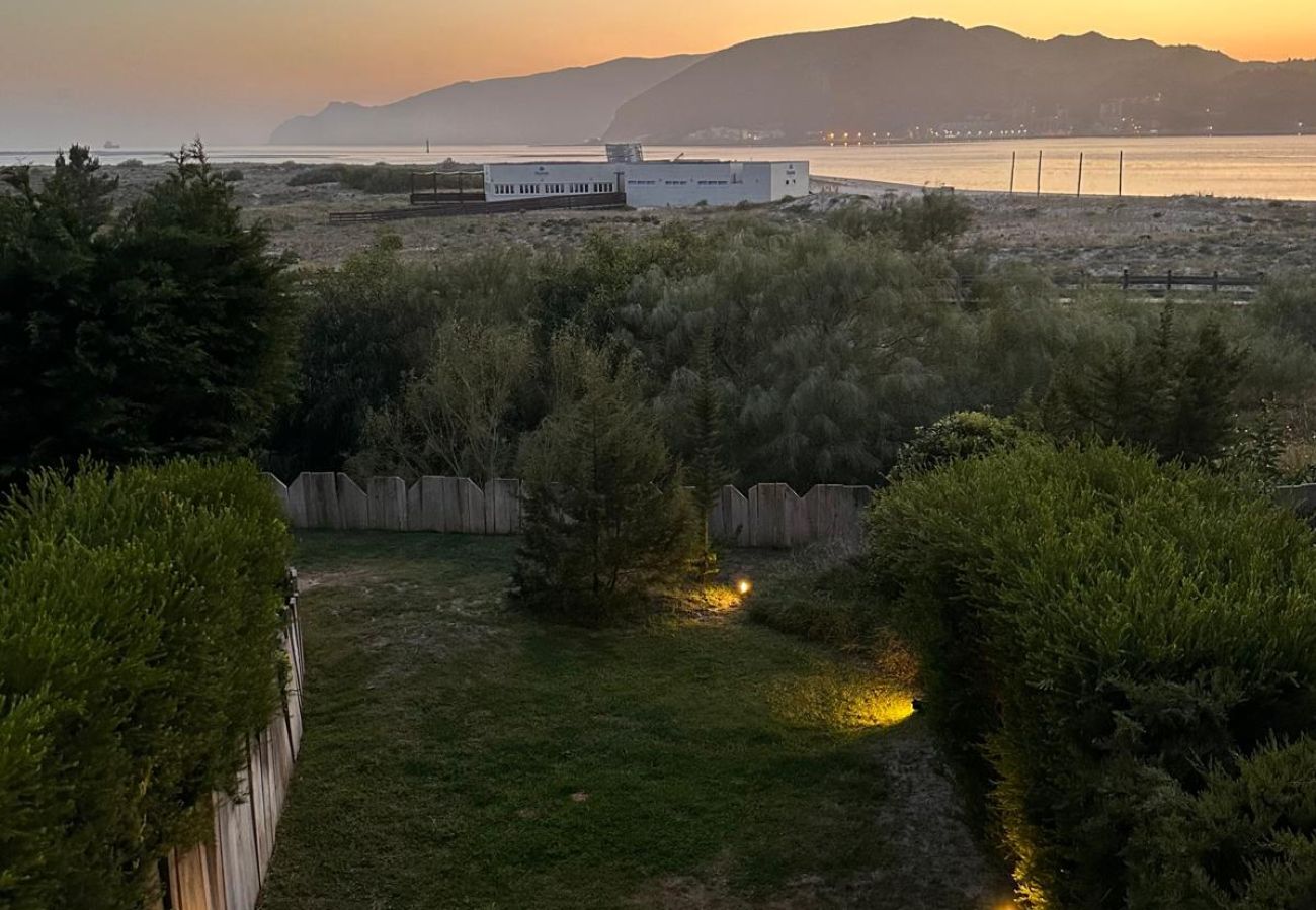 Jardim iluminado ao entardecer com vista para a vegetação, o mar e montanhas ao fundo.
