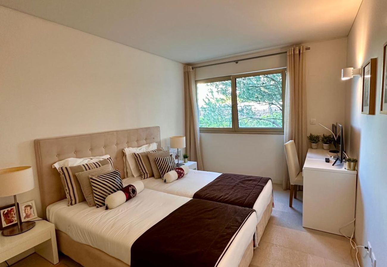 Quarto elegante e iluminado com duas camas de solteiro juntas, decorado em tons neutros. Conta com cabeceira estofada, almofadas decorativas, mesa de 