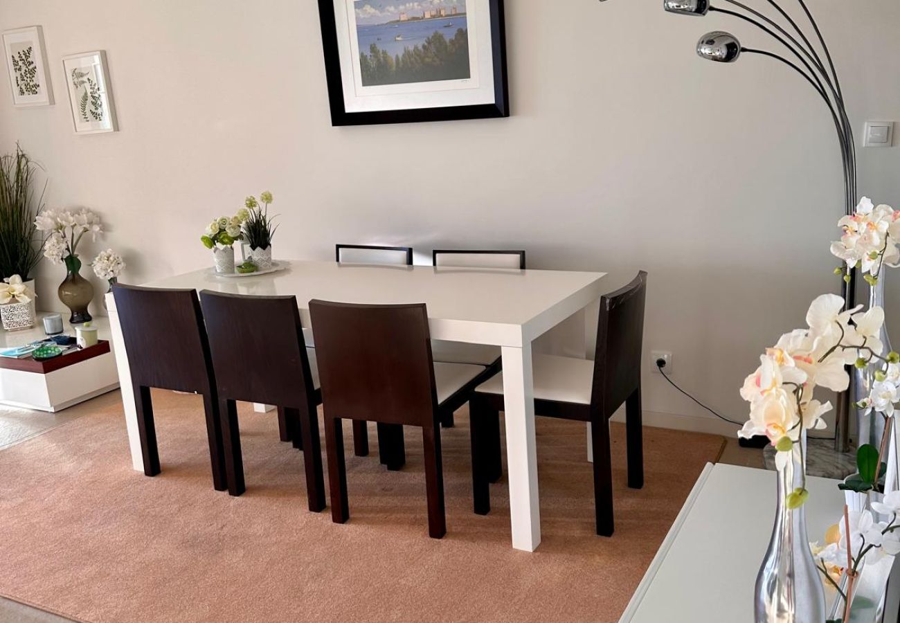 Sala de jantar espaçosa com mesa retangular de madeira, cadeiras estofadas escuras, tapete bege e luminária moderna de pé. Ambiente decorado com quadr