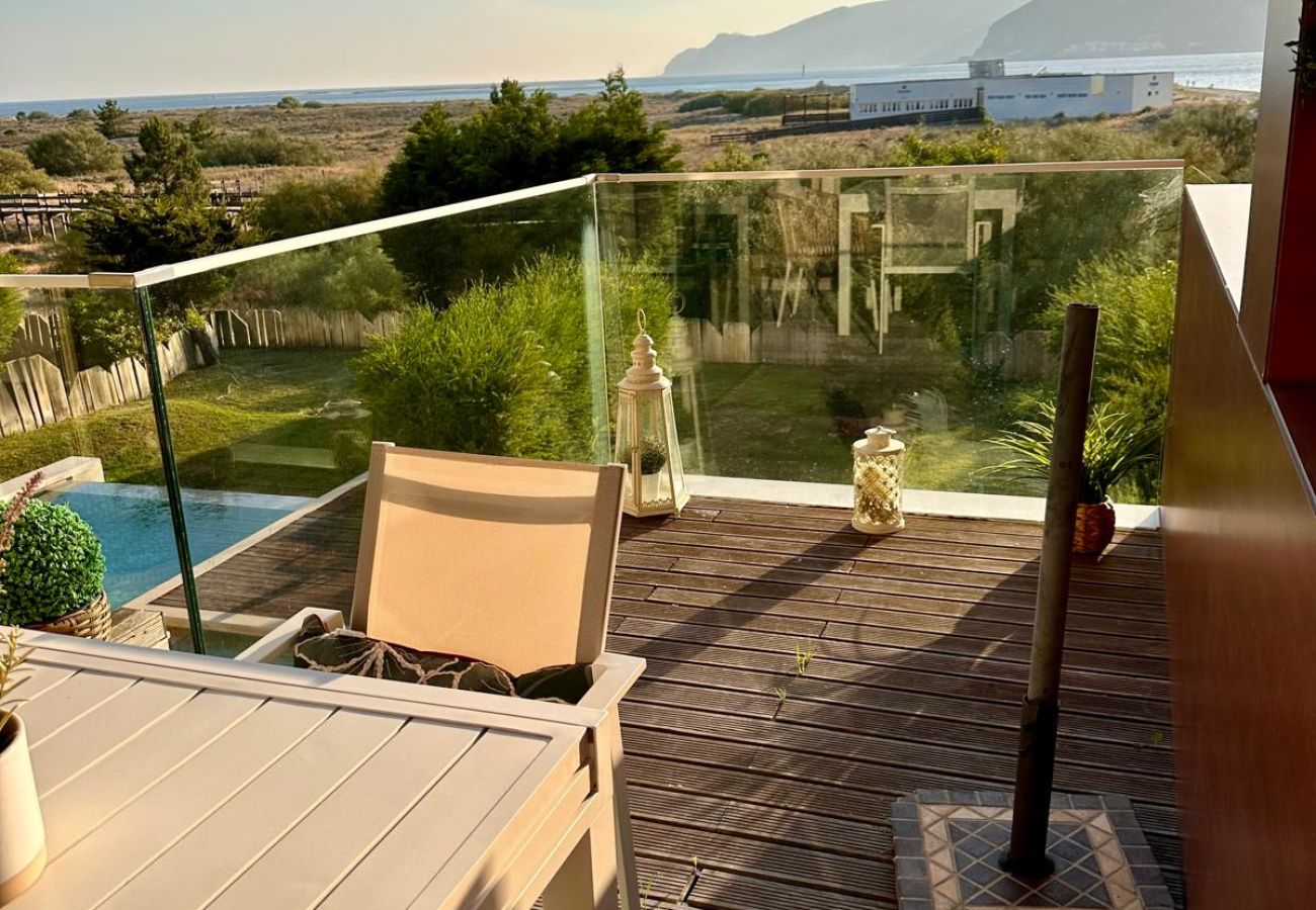  Varanda com mesa e cadeiras, vista para a natureza e montanhas ao fundo ao pôr do sol.