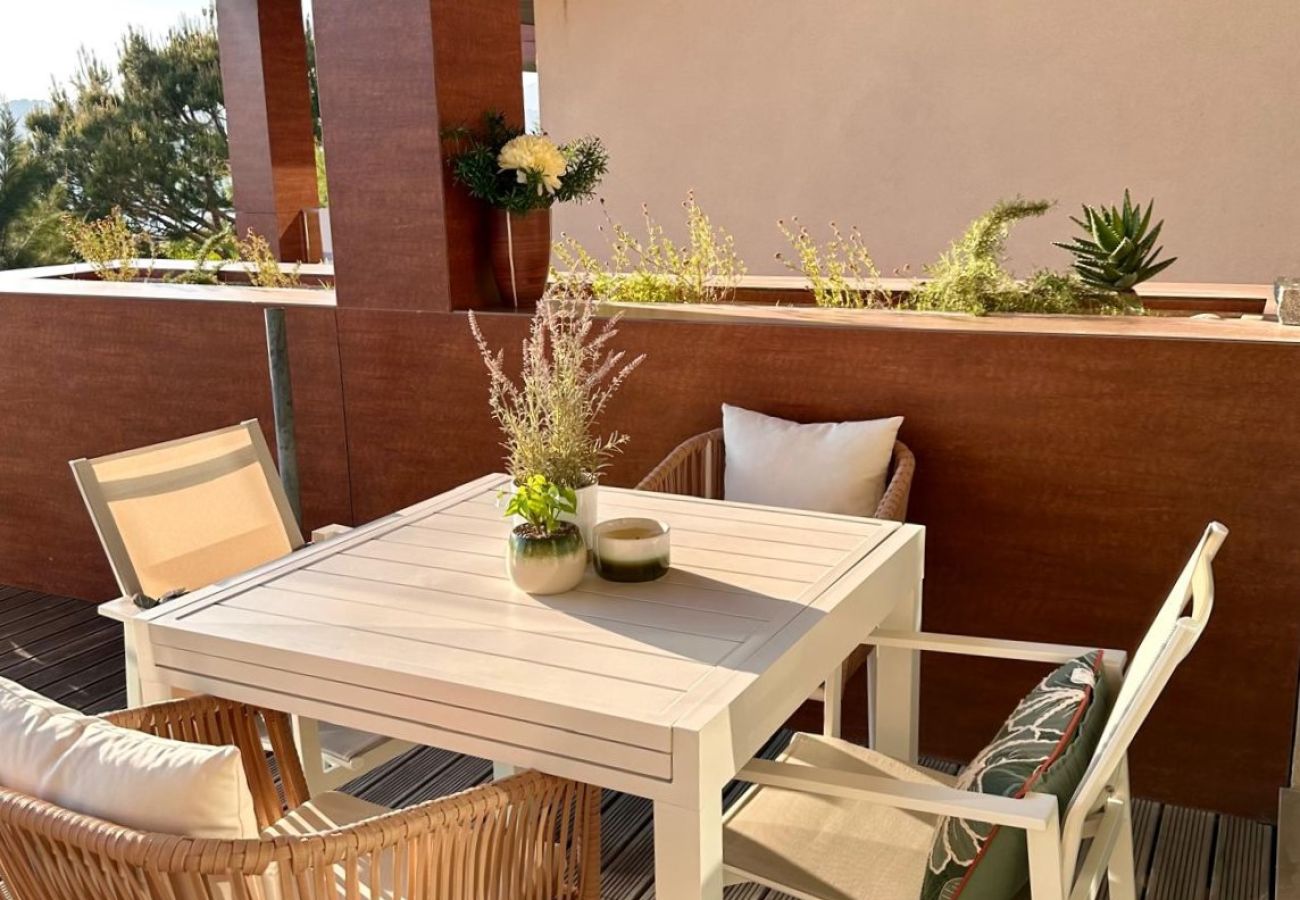 Espaçoso terraço ao ar livre com mesa de jantar branca, cadeiras elegantes e decoração com plantas verdes sob um teto de madeira.