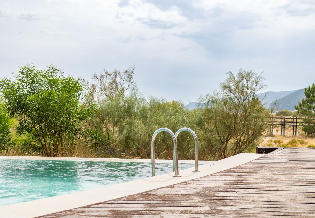  Piscina ao ar livre com escada metálica, rodeada por um deque de madeira e vegetação natural ao fundo.