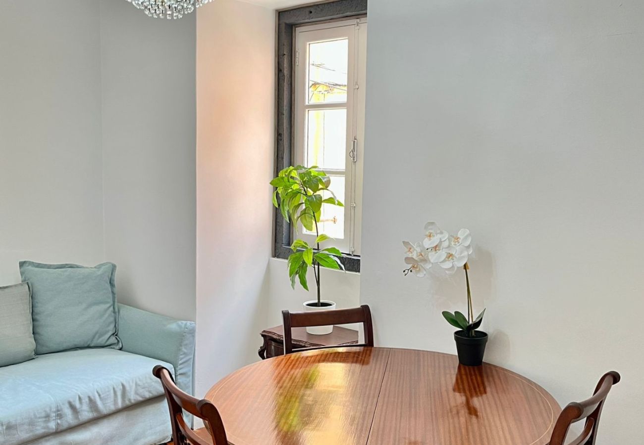 Sala de jantar aconchegante com mesa de madeira, cadeiras estofadas, televisão e lustre de cristal.