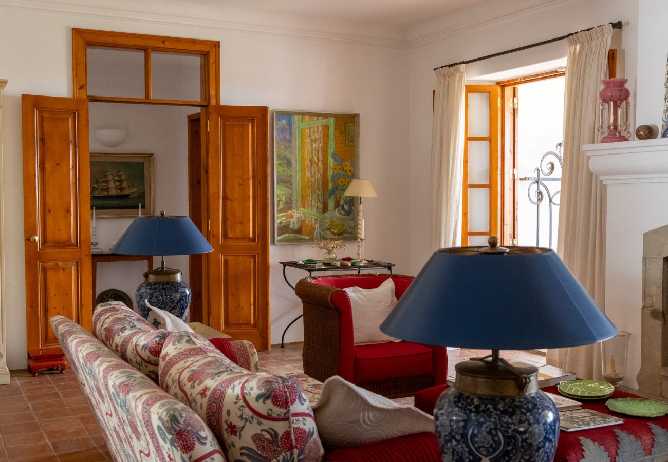 Sala de estar espaçosa com sofás estampados e vermelhos, luminárias de cerâmica azul, mesa de centro com livros e pratos decorativos, portas de madeir