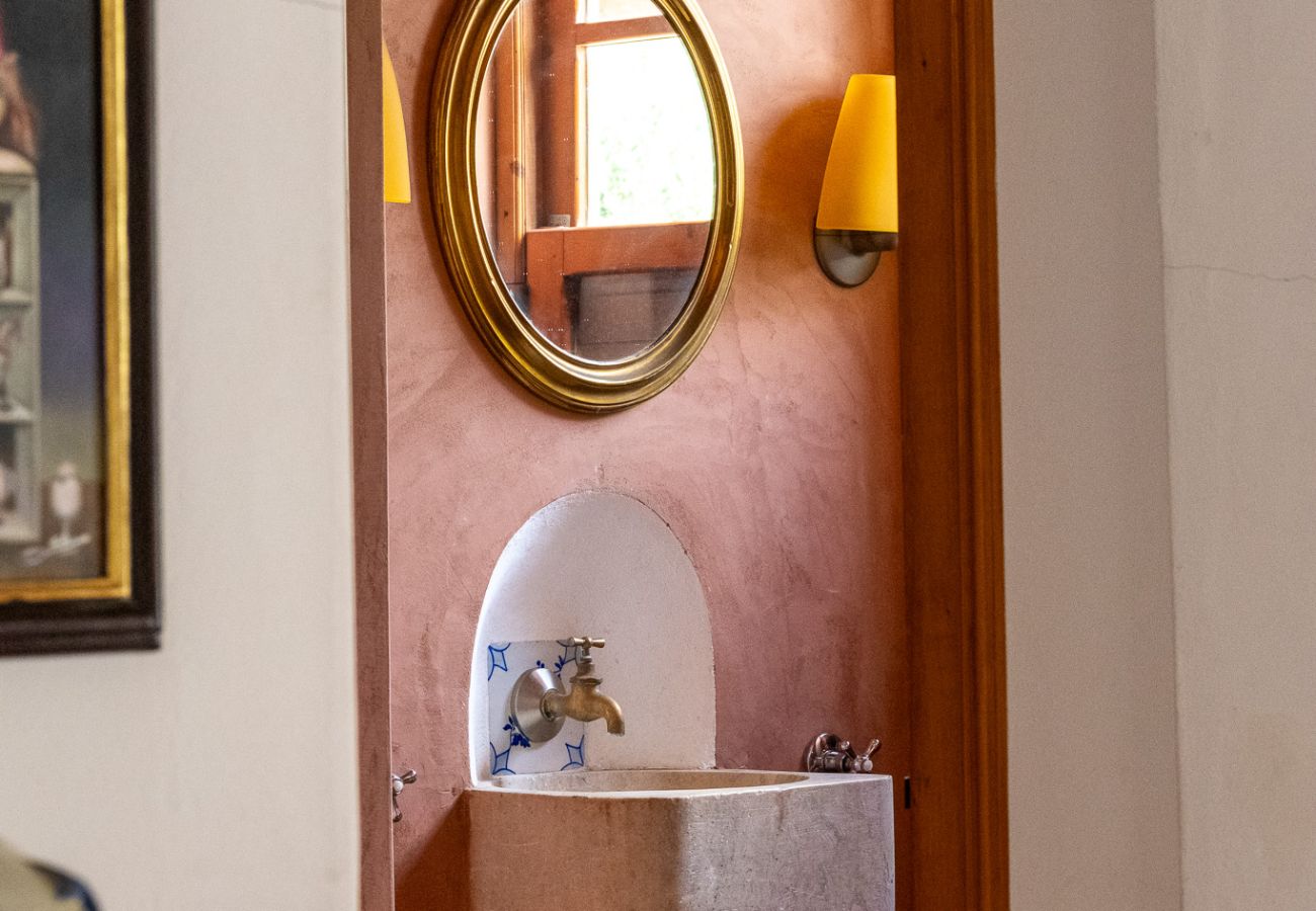 Pequeno lavabo com design rústico, espelho redondo dourado e lavatório de pedra.