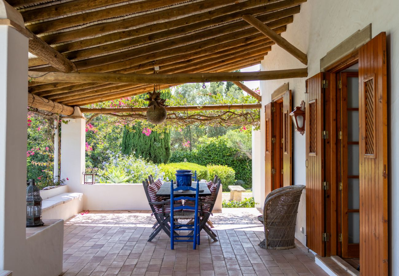 Varanda coberta com mesa de jantar, decoração rústica e vista para o jardim florido em Almancil.