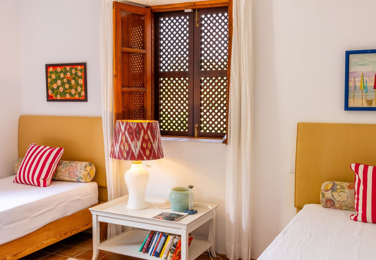 Quarto decorado com duas camas individuais de cabeceira amarela, almofadas listradas, abajur com estampa, mesa de cabeceira com livros e objetos decor