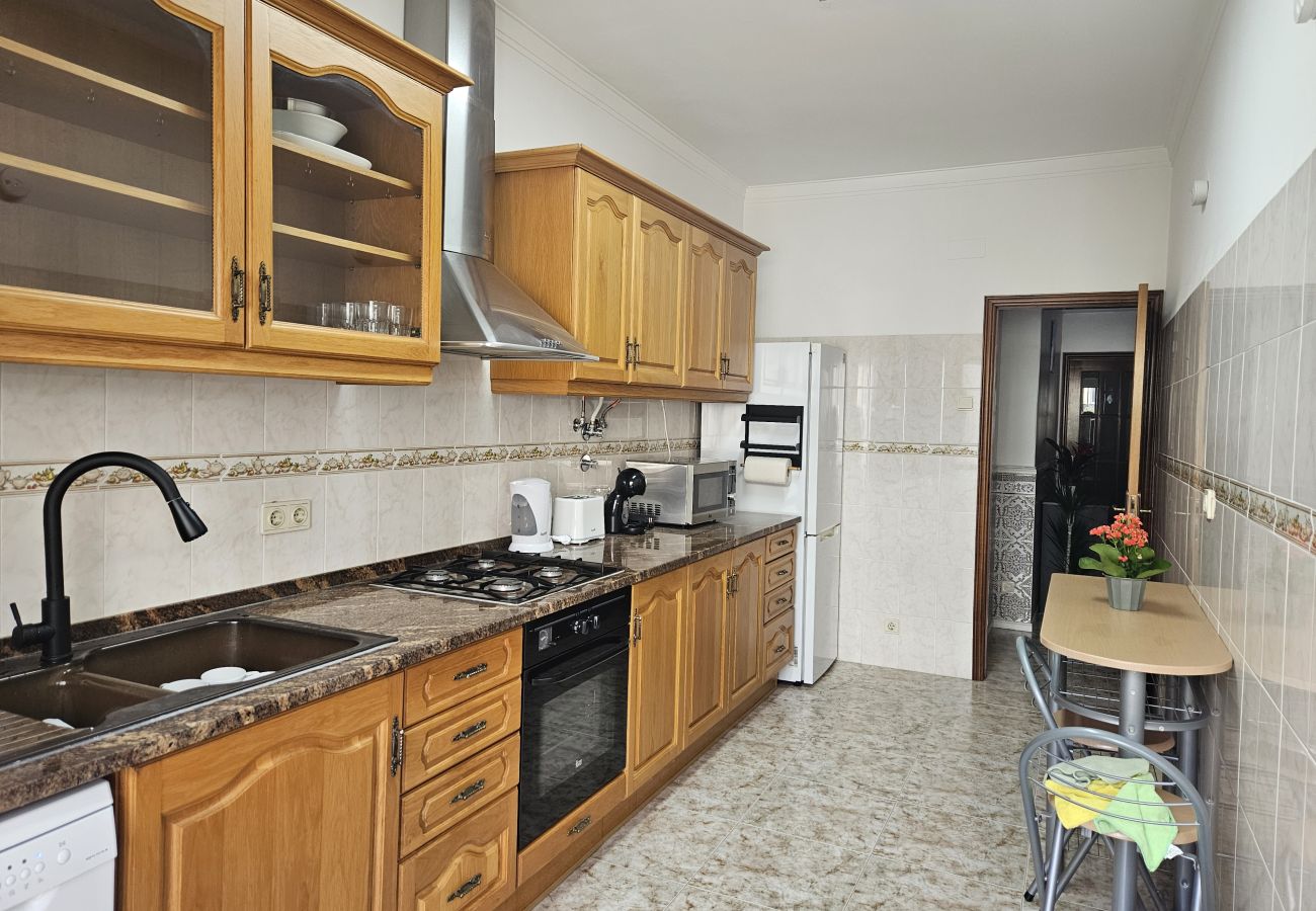 Cozinha ampla com armários de madeira, balcão de granito, eletrodomésticos modernos e mesa de refeições para duas pessoas.