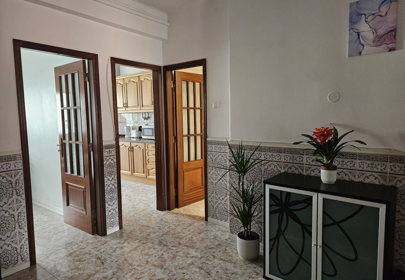 Entrada para a cozinha com portas duplas de vidro, parede com azulejos decorativos, armário preto moderno, plantas e um vaso de flores coloridas.