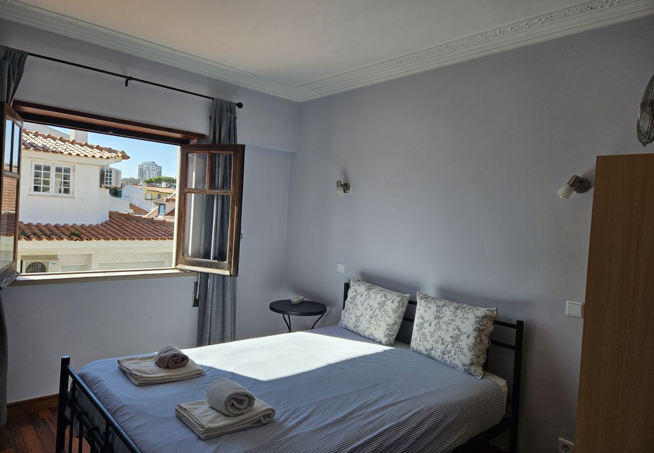 Double bed with white sheets, open windows and a view of the urban rooftops.