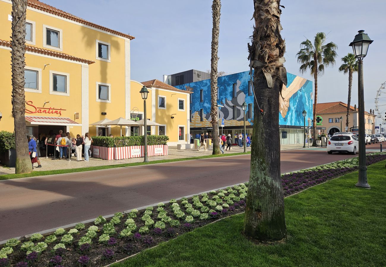 Charming avenue in Cascais, featuring palm trees, a well-maintained garden, colorful buildings, and an artistic mural in the background.