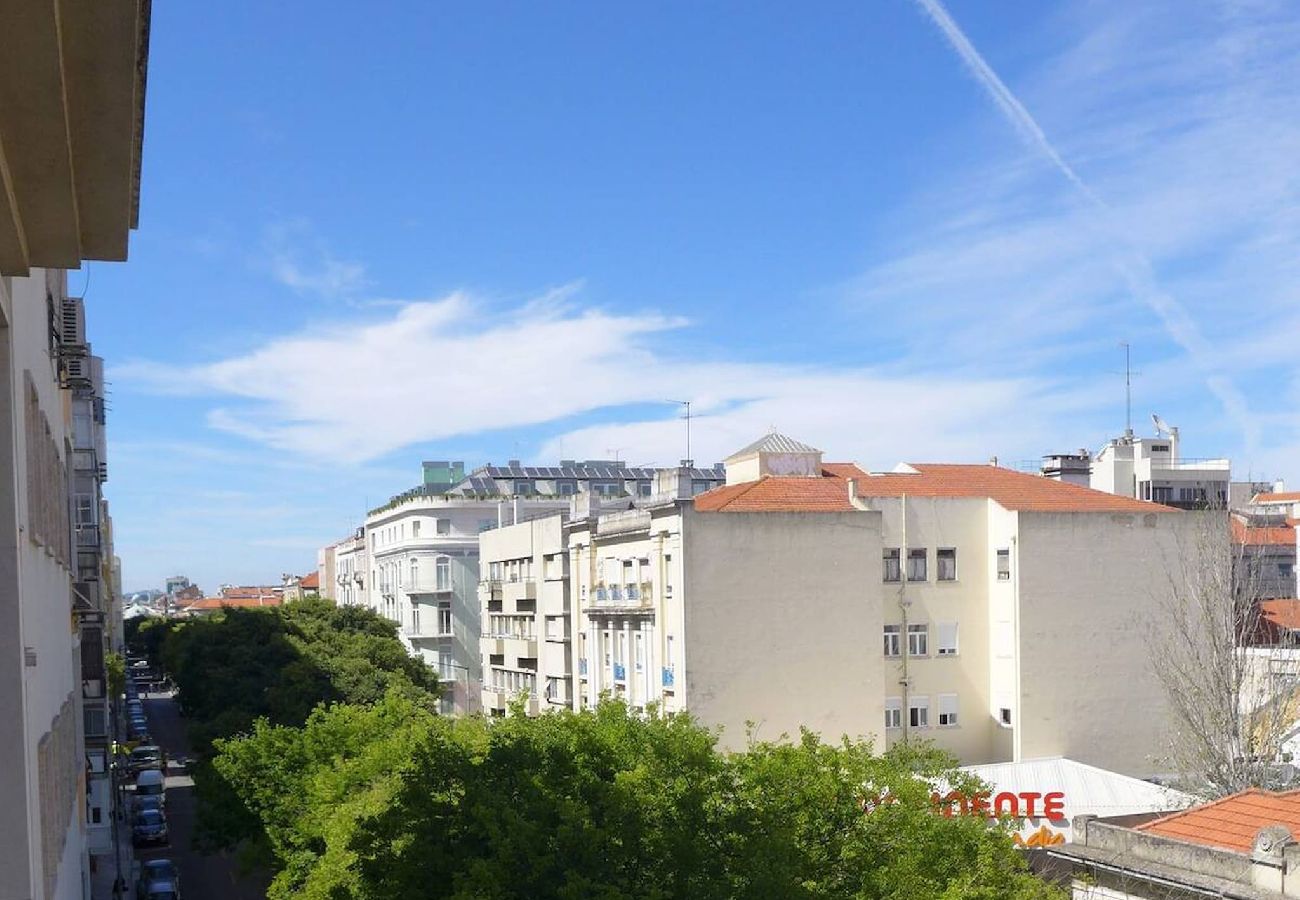 Tree-lined street with residential buildings and a blue sky with wispy clouds.