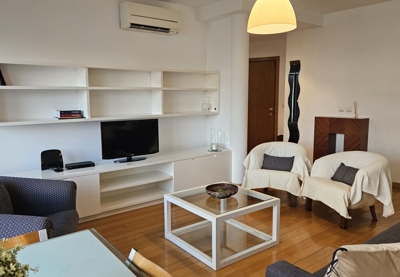 Living room with sofa, armchairs, modern white shelving unit, TV, and minimalist decor.
