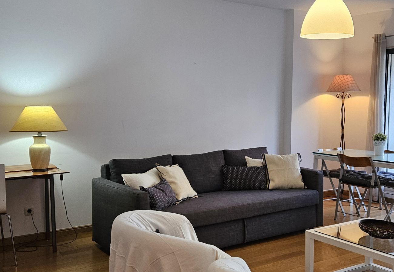 Room with elegant decor, comfortable sofa, white armchairs, dining table, and natural light from the balcony.