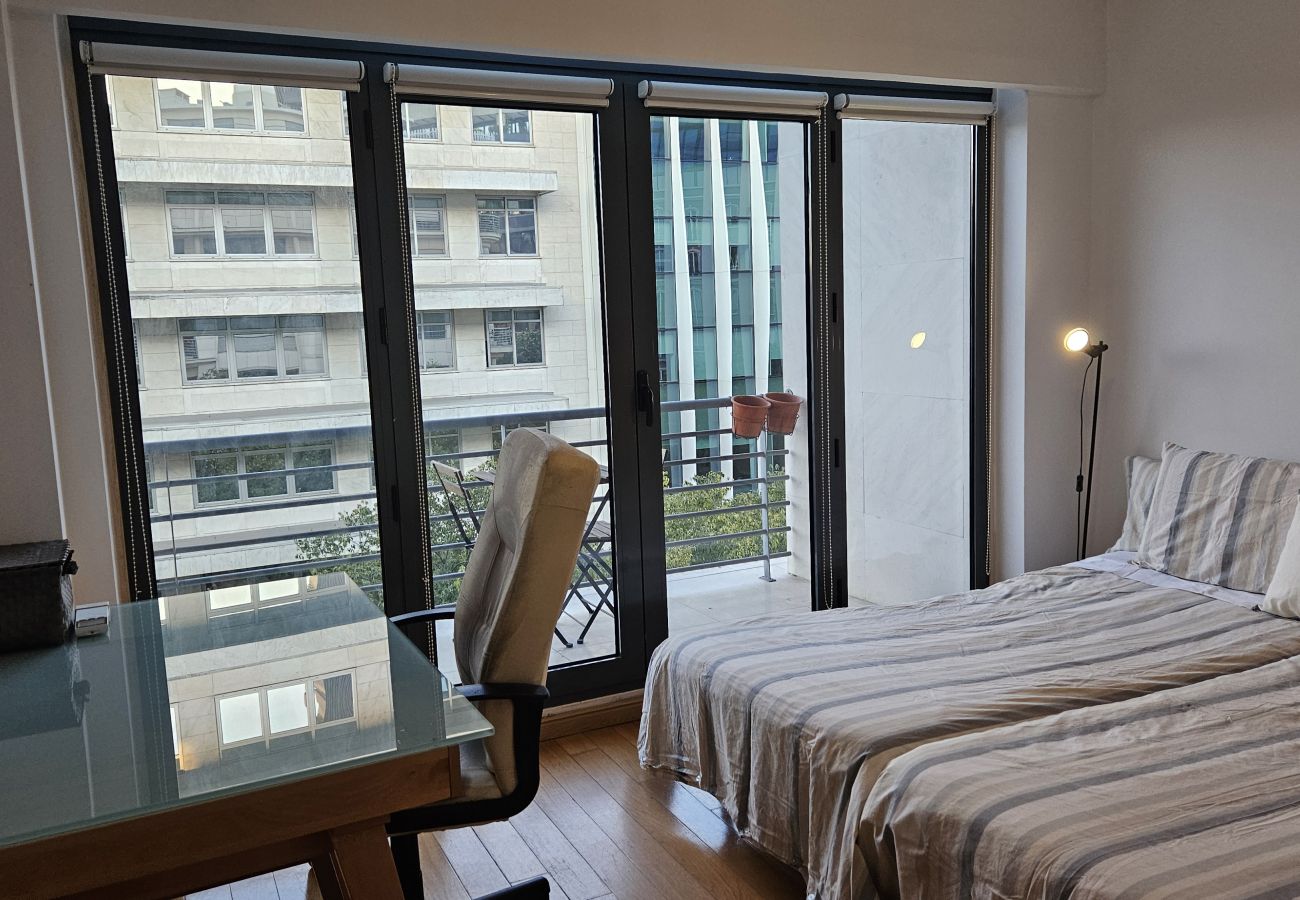 Cozy bedroom with a double bed, glass desk, and ergonomic chair next to the balcony.