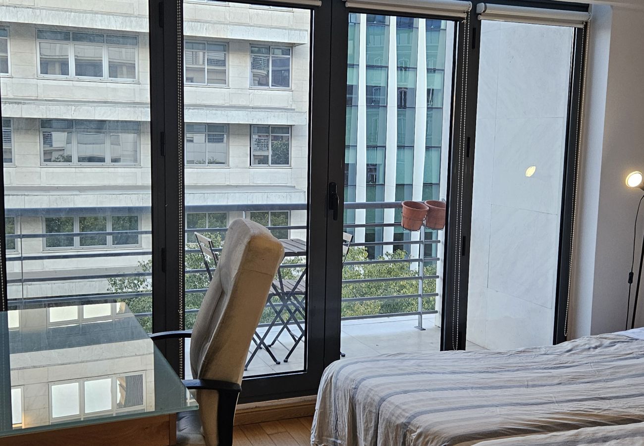 Spacious bedroom with a double bed, modern desk, and a balcony overlooking the city.