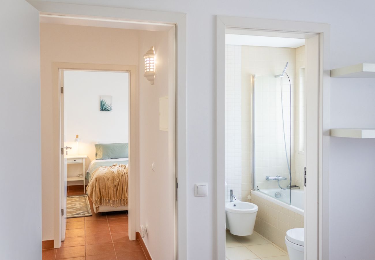 Bright hallway leading to a cozy bedroom and a modern bathroom with a bathtub.