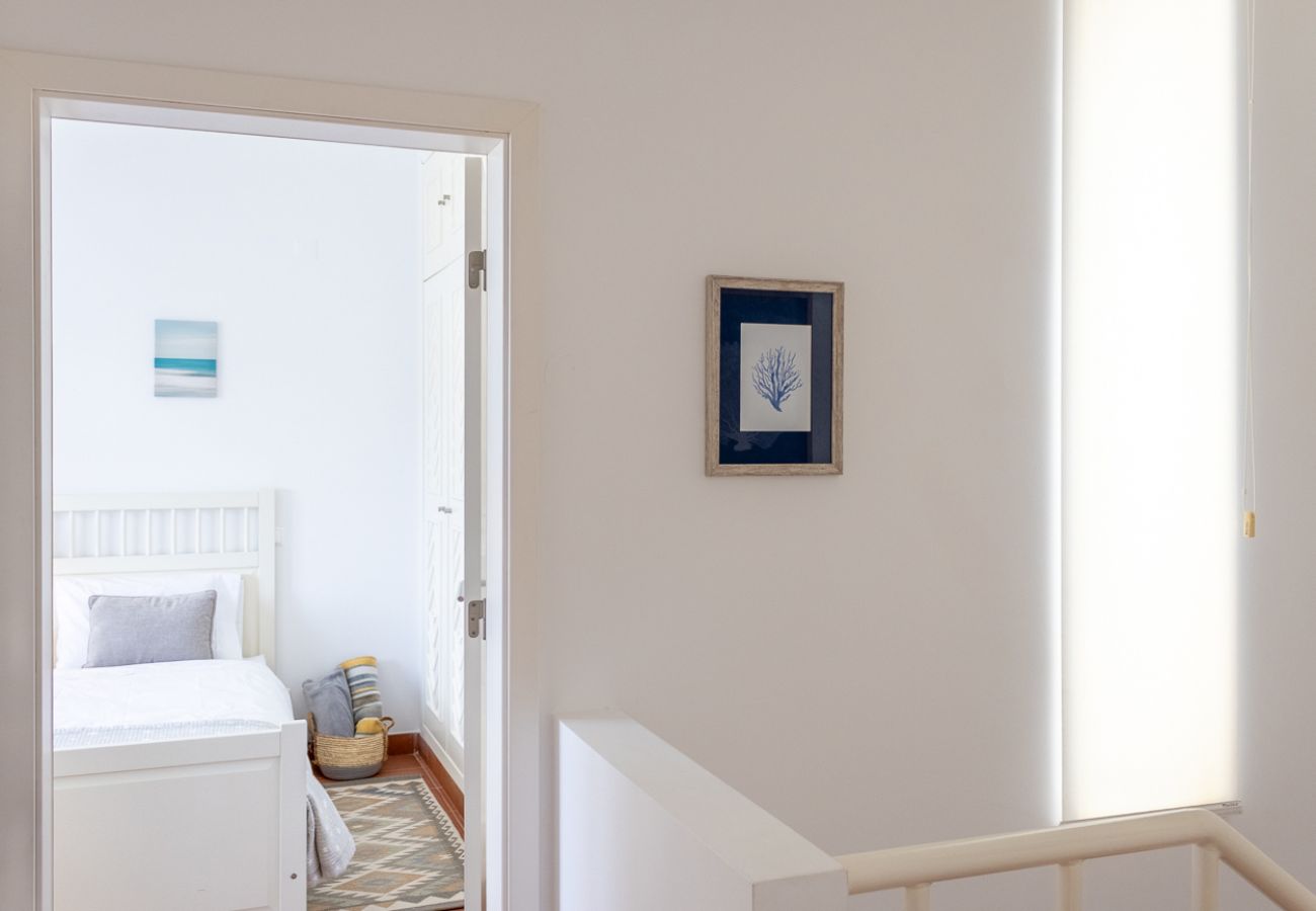 White hallway with natural light, decorative painting on the wall, and an open door leading to a bedroom with a white bed.