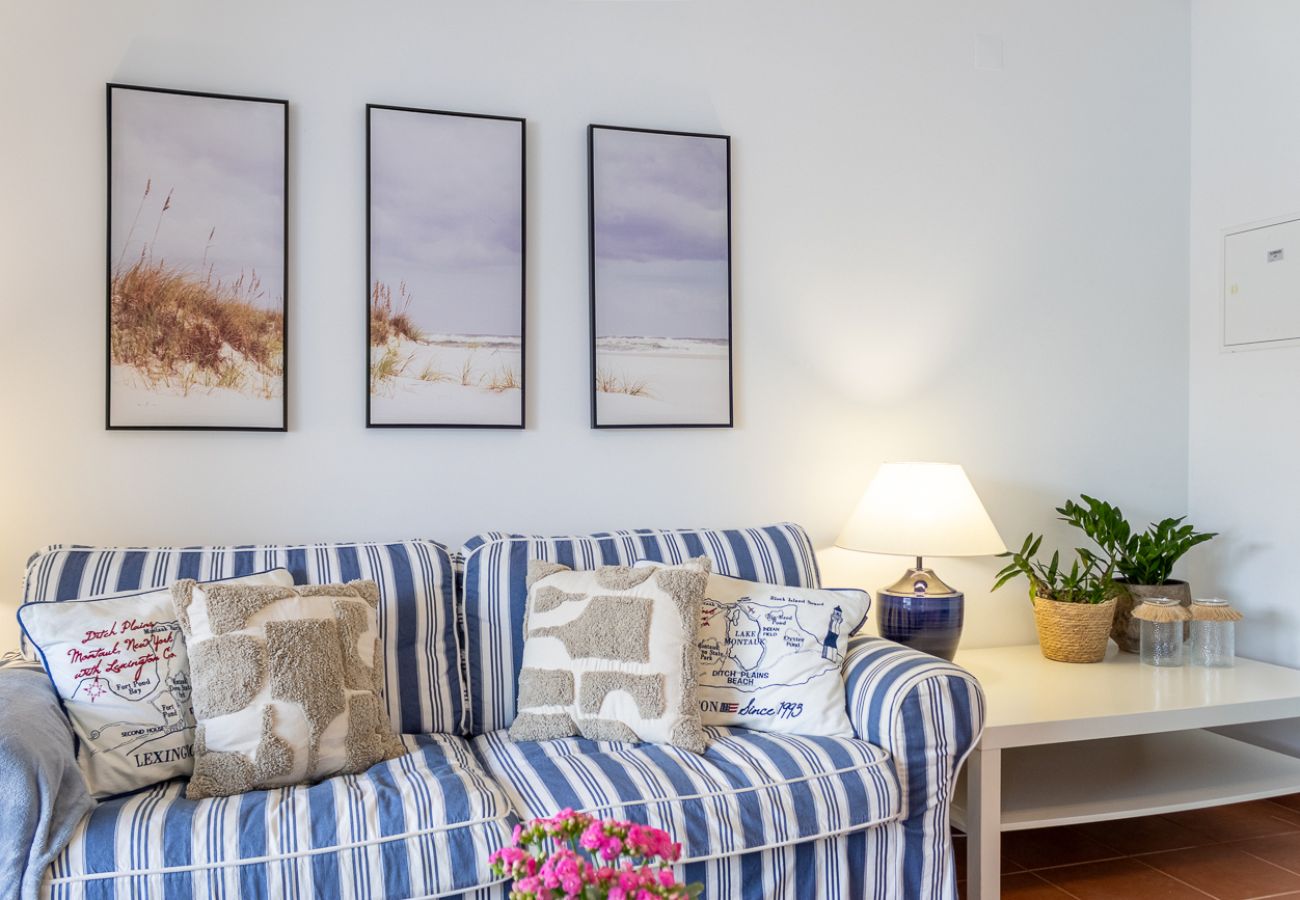  Living room with a blue and white striped sofa, decorative pillows, three landscape paintings on the wall, a lamp, and a side table with plants.