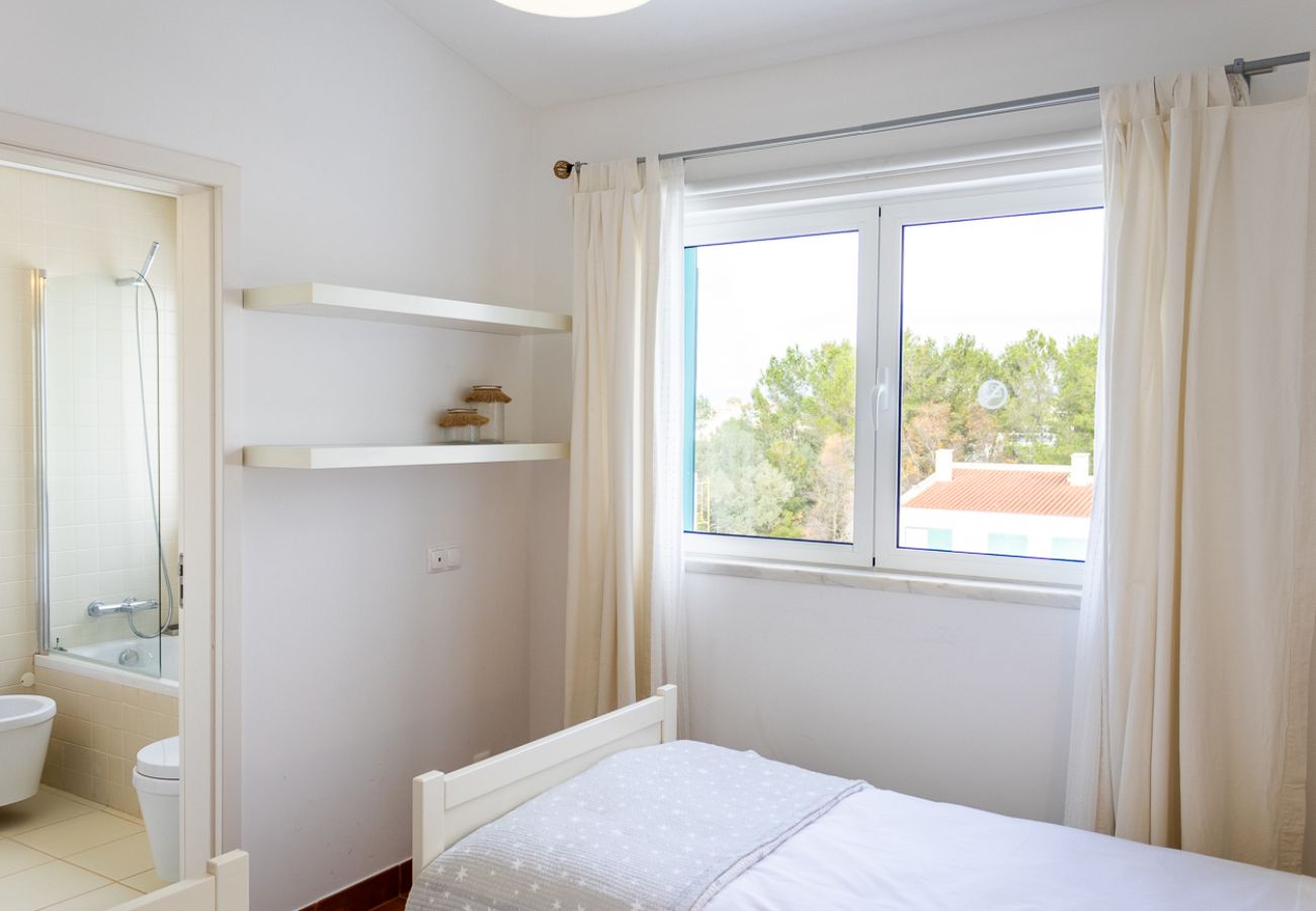Bedroom with a single bed, decorative shelves, large window with white curtains, and an outdoor view.